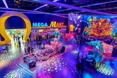 people are standing around in front of an exhibit with neon lights on the floor and large letters that spell out mega mart