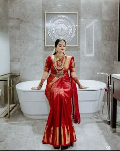 a woman in a red and gold sari is standing next to a bathtub