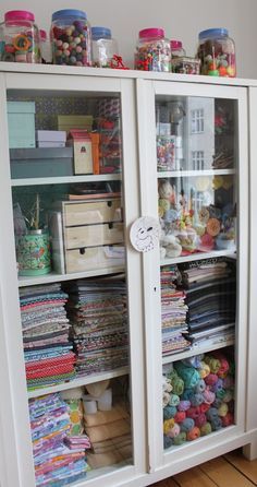 a white cabinet filled with lots of different types of fabric on top of wooden floors