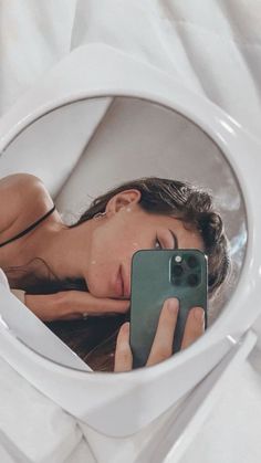 a woman taking a selfie in the mirror with her cell phone while laying down