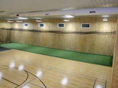 an indoor basketball court with wooden walls and green mats on the floor is pictured in this image