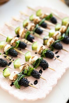 small skewered vegetables and blackberries are on a white plate with toothpicks