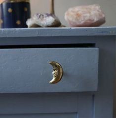 a close up of a drawer with a gold moon on the top and a blue vase in the background