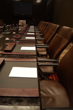 a long table with brown leather chairs and place mats on it in front of a projector screen