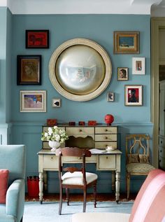 a living room with blue walls and pictures on the wall, including an antique desk