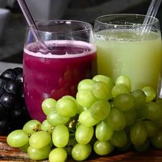 two glasses of juice and some grapes on a table