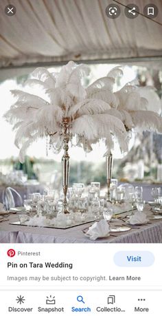 an image of a table set up for a wedding with white flowers and feathers on it