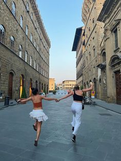 two women are dancing in the middle of an alleyway with brick buildings on either side