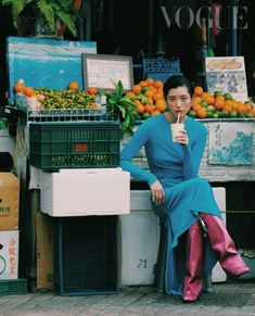 a woman sitting on a bench in front of fruit stand