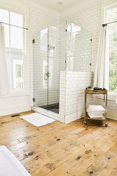 a bathroom with white brick walls and wood flooring is pictured in this image, there are two windows on either side of the shower