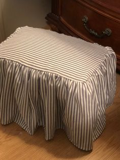 a striped bed skirt sitting on top of a wooden floor next to a chest of drawers