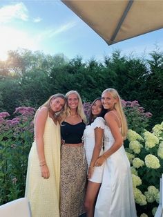 three women standing next to each other in front of flowers