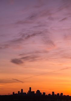 an airplane flying in the sky over a city with tall buildings and clouds at sunset