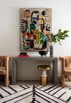 a living room with two chairs and a large painting on the wall above it's console table