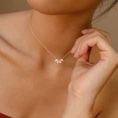 a woman wearing a gold necklace with two small white flowers on the end of it