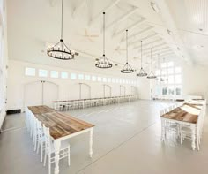 an empty room with tables and chairs in the center is lit up by hanging lights