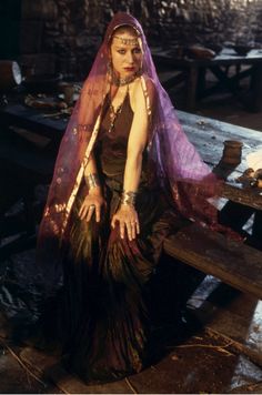 a woman sitting on top of a wooden bench wearing a purple and gold veil over her head