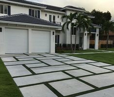 a driveway with grass in front of two houses and palm trees on the other side