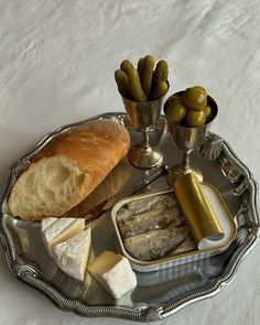 a silver tray with bread, cheese and pickles on it next to other food items