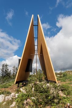 an unusual wooden structure sits in the middle of a grassy area with rocks and trees