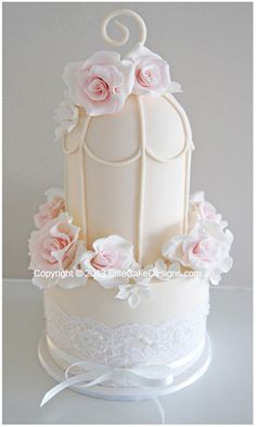 a white wedding cake with pink flowers on top and a birdcage decoration around the bottom