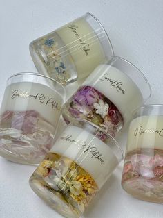 four clear cups filled with different types of flowers on top of a white countertop