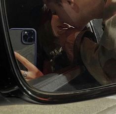 a man taking a selfie in the side mirror of a car with his cell phone