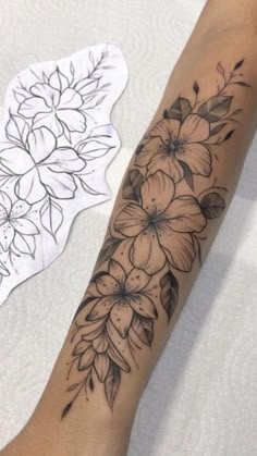 a woman's arm with flowers on it next to a white piece of paper