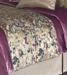 a bed with purple and gold comforter on top of it's headboard