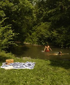 two people are swimming in the water near a blanket and picnic cloth on the grass