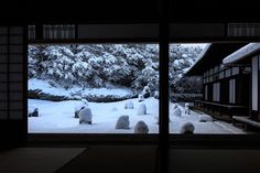 snow covered rocks in front of an open window with trees and bushes on the other side