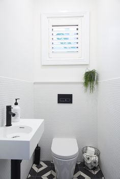 a white toilet sitting next to a sink in a bathroom under a window with shutters