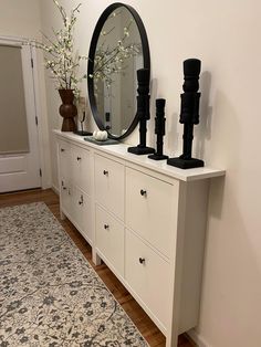 a white dresser topped with black vases next to a mirror