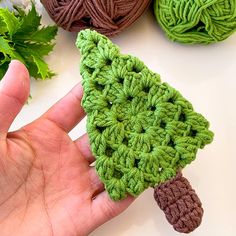 a hand holding a green crocheted turtle on top of two balls of yarn