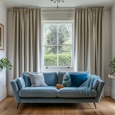 a blue couch sitting in front of a window with drapes on the windowsill