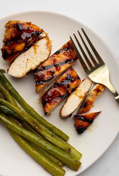 grilled chicken and green beans on a white plate with a fork next to it