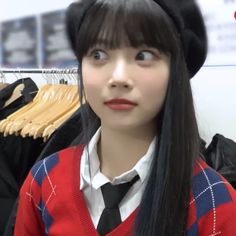 a girl with long black hair wearing a sweater and tie