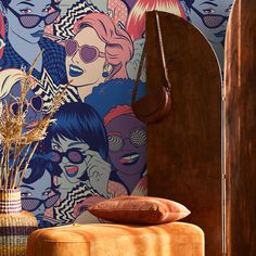 a colorful wallpapered room with an orange ottoman and wooden floor lamp next to it