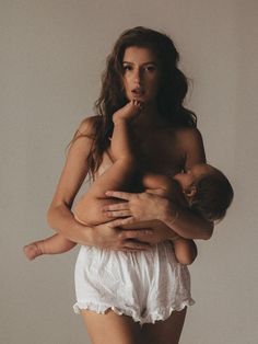 a woman holding a baby in her arms and posing for the camera with no shirt on