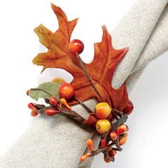 an orange and yellow leaf is on top of a white napkin with berries, leaves and acorns