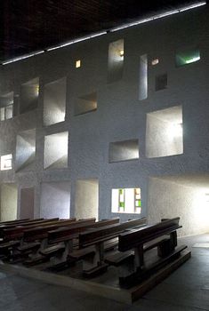 an empty church with rows of pews in front of the windows and lights on the wall