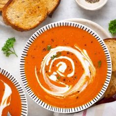 two bowls of tomato soup with bread on the side