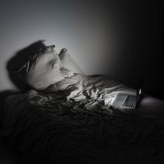 an open laptop computer sitting on top of a bed in the dark with sheets and pillows