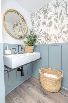 a white sink sitting under a bathroom mirror next to a wooden basket filled with plants