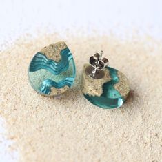 there are two earrings on the sand and one is in the shape of a wave