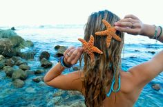 a woman standing next to the ocean holding two starfishs in her hair and wearing bracelets