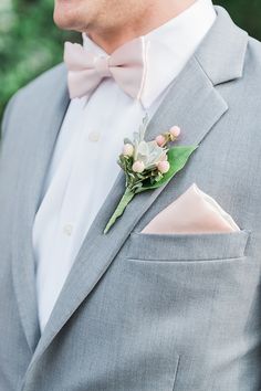 a man wearing a gray suit with a pink bow tie and boutonniere