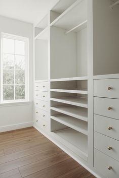 an empty white closet with wooden floors and drawers