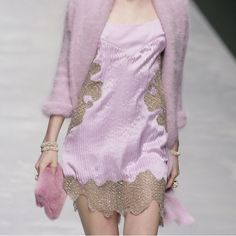 a woman walking down a runway wearing a pink dress and jacket with gold trimmings