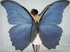 a woman in a white dress with a blue butterfly on her back and wings spread out